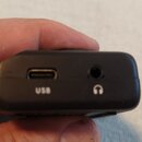 Detailní pohled na černý plastový konec elektronického zařízení. Jsou zde vidět dva porty: USB-C s nápisem USB a jackový vstup pro sluchátka s ikonou…