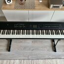 Černý digitální klavír na černém X-stojanu. Na levé straně je bílý nápis Roland RD-800. Horní panel obsahuje displej, ovládací knoflíky a tlačítka. N…
