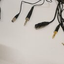 Fotografie zobrazuje sadu černých audio kabelů s různými konektory. Jsou zde vidět konektory typu XLR, 6,3mm jack a RCA (červený a bílý). Na kabelech…