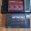 Červený basový efektový procesor s nápisem ZOOM B3n Bass Multi-Effects Processor. Je umístěn na černém podložkovém kufru značky ZOOM spolu s napájecí…