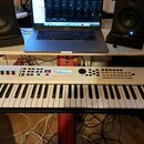 Bílá klávesová syntezátor s černými klávesami a ovládacím panelem. Na levé straně je logo YAMAHA a na pravé nápis MX61. Nástroj je umístěn na červené…