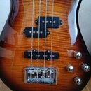 Detail těla elektrické basové kytary s lakovaným povrchem z dřeva s výraznou kresbou zrn. Nástroj má dva snímače typu humbucker v černé barvě a tři c…