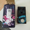 Černý efekt pedál s nápisem REVERB a modrým grafickým motivem planety. Na horní části jsou dva černé ovládací knoflíky s popisky DECAY a MIX, přepína…