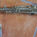 Detailní pohled na horní část saxofonu v lakovaném zlatém provedení. Nástroj vykazuje známky opotřebení v podobě drobných škrábanců a znečištění povr…