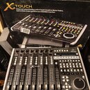 Fotografie zobrazuje kontrolní plochu Behringer X-TOUCH v originální krabici. Zařízení je černé s kovovými bočními listy, obsahuje 9 motorických posu…