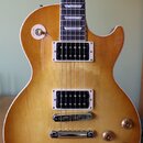 Elektrická kytara s trupem v žlutém přechodovém odstínu (burst) a bílým lemováním. Nástroj má dva humbuckery s bílými rámečky, čtyři zlaté ovládací k…