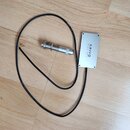 Na fotografii je stříbrný obdélníkový snímač s nápisem KRIVO PICK-UPS a připojený černý kabel. K kabelu je připojena stříbrná kovová součástka, pravd…