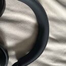 Černá bezdrátová sluchátka s polstrováním náušníků a čeleny z textilního materiálu. Povrch je v dobrém stavu bez viditelného opotřebení. Na fotografi…