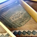Detailní pohled na vnitřek klavírního nástroje s viditelnými kovovými strunami a dřevěnými prvky. Pod strunami je na dřevěném povrchu viditelný nečit…