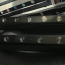Dvě černé lineární LED lampy s řadou kulatých čoček. Jsou umístěny vodorovně jedna nad druhou na tmavém rýhovaném povrchu. Na přístrojích nejsou vidě…
