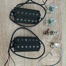 Dva černé humbuckery s černými kryty snímačů a viditelnými polosférickými póly. K oběm snímačům vedou černé kabely s barevnými vodiči. Vedle nich jso…