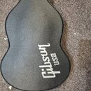 Černý tvarový pouzdro na kytaru s texturovaným povrchem. Uprostřed je bílý nápis Gibson a pod ním menší nápis USA. Povrch pouzdra vykazuje mírné znám…