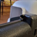 Detailní záběr na černý, texturovaný plastový obal nebo pouzdro. V horní části je viditelné výrazné poškození materiálu ve formě trhliny a odloupanéh…