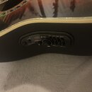 Detailní pohled na ovládací panel akustické kytary s černým povrchem. Na panelu jsou nápisy TUNE, BATT. LOW a EQ s posuvníky označenými MAX, LOW, MID…