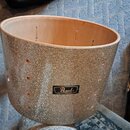 Stříbrný buben s glitrovým povrchem. Na přední straně je černý obdélníkový štítek s bílým nápisem Pearl. V horní části korpusu jsou vidět otvory pro…