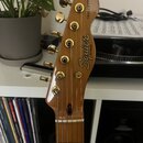 Fotografie zachycuje hlavu elektrické kytary v hnědé barvě s osmoticým povrchem. Na hlavě je zlaté logo Squier BY FENDER a nápis TELECASTER®. Nástroj…