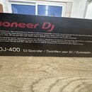 Fotografie zachycuje část kartonového obalu od DJ kontroléru. Na černé ploše je bílým a červeným písmem nápis Pioneer Dj a modelové označení DDJ-400…