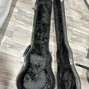 Otevřený tvrdý kufýr na kytaru v černé barvě. Vnitřní prostor je vyložen černým plyšovým materiálem, který vykazuje známky opotřebení a zplstnatění.…