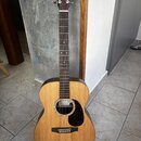 Akustická kytara s přírodním dřevem a tmavým hmatníkem. Na hlavě je logo Martin & Co EST. 1833 a uvnitř ozvukové otvory je štítek s nápisem X Series.…