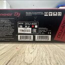 Fotografie znázorňuje zadní stranu kartonového obalu od DJ kontroléru. Na krabici je výrazný nápis Pioneer DJ a modelové označení DDJ-400. Na bílém š…