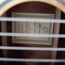 Fotografie zachycuje vnitřek akustické kytary s viditelnou štítkem uvnitř korpusu. Na štítku je uveden nápis ORTEGA GUITARS EST 1934, FAMILY SERIES P…