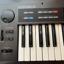 Černý digitální klavír značky Roland. Na ovládacím panelu je velký otočný ovladač s nápisem α-DIAL, posuvník VOLUME a kola PITCH BENDER s nápisem MOD…