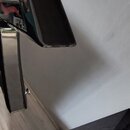Detailní záběr na černý, lesklý povrch části hudebního nástroje. Na hraně horního dílu je viditelné odloupaní laku a opotřebení povrchu. Žádné značky…