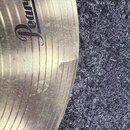 Detailní záběr na okraj kovového činele zlaté barvy s viditelným logem Pearl. Na povrchu je v pravé části patrná prasklina sahající od okraje směrem…