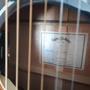 Fotografie zachycuje vnitřek korpusu akustické kytary z pohledu skrz otvory pro struny. Uvnitř je nalepený bílý štítek s nápisy Sigma Guitars EST. 19…
