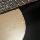 Detailní záběr na hmatník a horní desku akustické kytary. Hmatník je z tmavého dřeva s kovovými pražci, horní deska je ze světlého dřeva s černým pic…