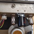 Fotografie zachycuje vnitřek zesilovače s kovovým šasi, na kterém jsou osazeny dvě elektronky a jeden černý kondenzátor. Na jedné z elektronek je svi…