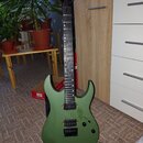 Elektrická kytara s matně zeleným povrchem korpusu a černým hmatníkem. Nástroj má dva humbuckery, jeden ovládací knoflík a přepínač. Kytara je umístě…