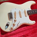 Bílá elektrická kytara typu Stratocaster s bílým pickguardem a třemi jednoduchými snímači. Na ovládacích knoflících jsou nápisy VOLUME a TONE. Nástro…