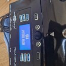 Černý procesor efektů značky TC HELICON z řady play ACOUSTIC. Zařízení má digitální displej s modrým podsvícením, na kterém je nápis HOW GREAT 113. N…
