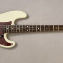 Elektrická basová kytara s krémovým povrchem těla a hnědým hmatníkem. Na hlavě je viditelné logo Fender a nápis PRECISION BASS. Nástroj má vínový pic…