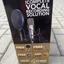 Fotografie znázorňuje kartónovou krabici s produktem. Na ní je nápis THE COMPLETE VOCAL RECORDING SOLUTION a obrázek mikrofonu v šokmountu s popfiltr…
