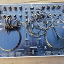 Modrý DJ kontrolér značky Reloop s bílým rámem. Na spodní části je nápis JOCKEY MIX a logo TRAKTOR BEAT, vprostřed je logo RELOOP. Přes přístroj jsou…