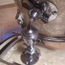 Detailní záběr na chromovaný držák bubnu s připevněným tomem. Povrch nástrojů má světle béžový perleťový vzhled. Na horním kovovém držáku je svisle v…