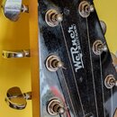 Detail hlavy černé kytary s chromovanými ladičkami. Uprostřed je bílý nápis „Werner GUITARS“. Povrch laku vykazuje četné drobné škrábance a prachové…
