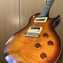 Elektrická kytara s prohnutým topem z plamenového javoru v žlutě-hnědém sunburst provedení. Nástroj má dva humbuckery v krémových rámečcích a čtyři o…