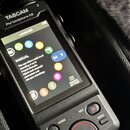 Černý digitální záznamový zařízení s barevným displejem. Na horní části je bílý nápis TASCAM a pod ním model Portacapture X8. Displej zobrazuje menu…