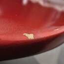 Detailní záběr na červený lakovaný povrch hudebního nástroje. V popředí je vidět výrazný odlak v podobě světlého škrábance nebo odštípnuté vrstvy lak…