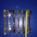 Šest kusů kovových chromovaných držáků na nástroje, pravděpodobně mechanismy pro ladění nebo upevnění. Jeden z kusů je černý s mosaznými šrouby, osta…