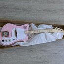 Růžová elektrická kytara s bílým pickguardem v hnědé kartonové krabici, vyložená bílou látkou. Na hlavě hmatníku je viditelné logo JoJo. Nástroj má d…