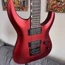 Elektrická kytara s červeným matným povrchem a hnědým hmatníkem. Nástroj má dva černé humbuckery a černý most s integrovaným pákovým systémem. Na těl…