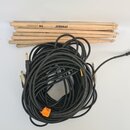 Na fotografii je svázek dřevěných bubeníckých paliček a smotaný černý kabel s jack konektory. Na horní paličce je čitelný nápis DYNABEAT 5B U.S. HICK…