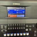 Detailní pohled na ovládací panel a displej klávesového nástroje značky YAMAHA. Na barevném displeji jsou vidět nápisy Regist, NewBank, Mic Setting,…