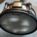 Černý tréninkový buben s kovovými obručemi a stahovacími šrouby. Na bílém membráně je nápis Roland MESH HEAD made by REMO a ve spodní části PowerPly…