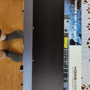 Černý rackový procesor s nápisem VOICEWORKS HARMONY CORRECTION EFFECTS. Na zařízení je umístěna černá ochranná krytka a žlutý varovný štítek. Zařízen…