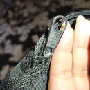 Detailní záběr na černý zip z textilního materiálu. Na jezku zipu je vyryt nápis KL. Materiál v okolí zipu vykazuje známky opotřebení a rozestřepené…